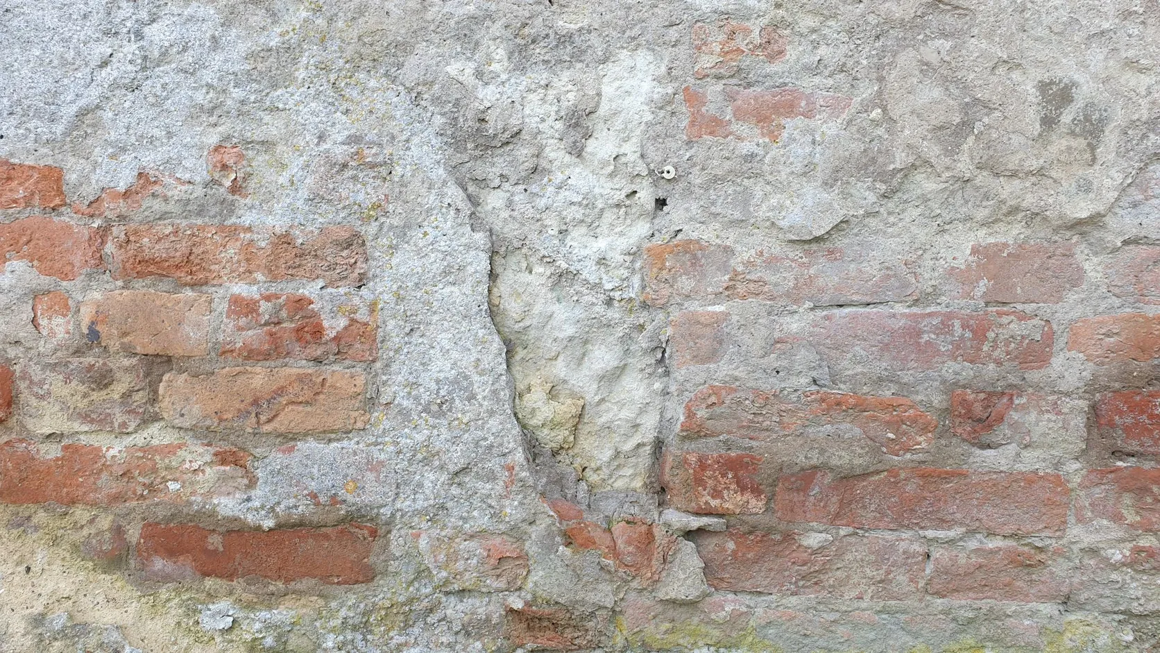 Gros plan d'un vieux mur de briques rouges dont l'enduit gris s'écaille et se fissure