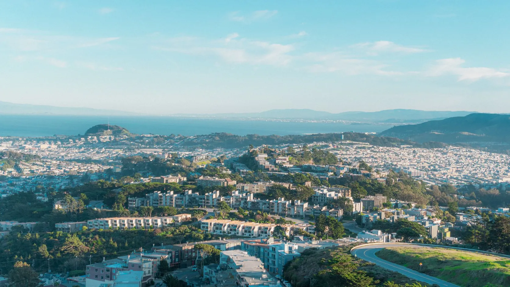 Quartiers résidentiels de San Francisco vus d'une colline, avec la baie et les reliefs au loin sous un ciel bleu