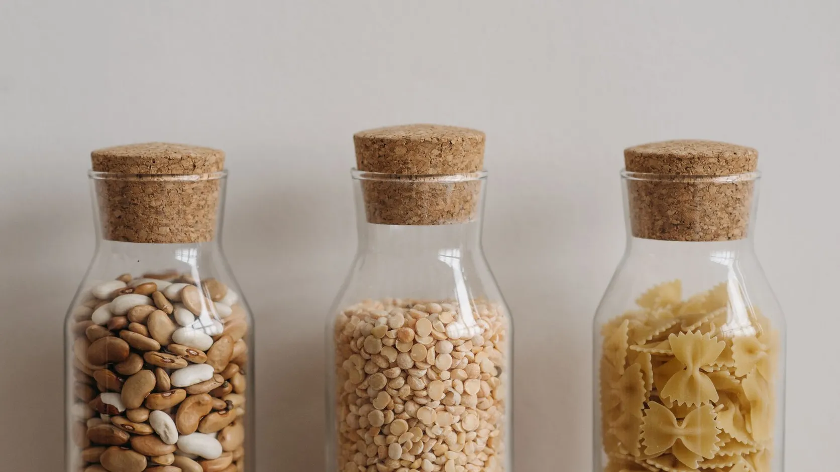 Trois bocaux en verre fermés par des bouchons en liège, remplis de haricots secs, de pois cassés et de pâtes papillons