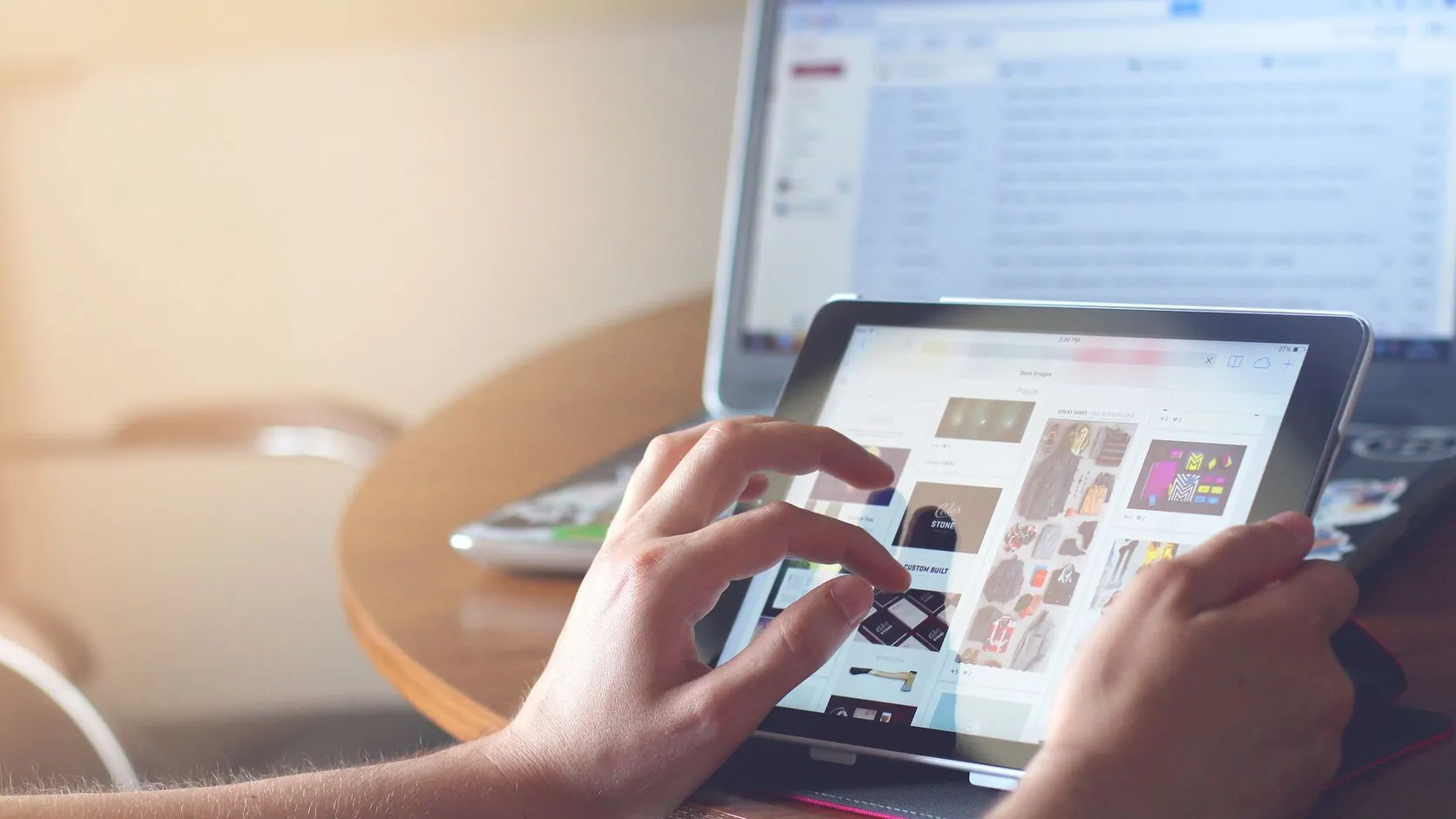 Mains qui font défiler une page web sur une tablette, devant un ordinateur portable affichant une boîte de réception