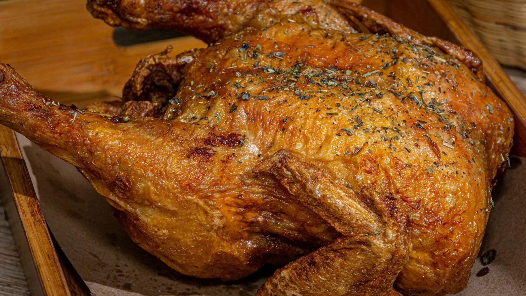 Poulet entier rôti à la peau dorée, saupoudré d'herbes séchées, posé sur un papier dans une caisse en bois