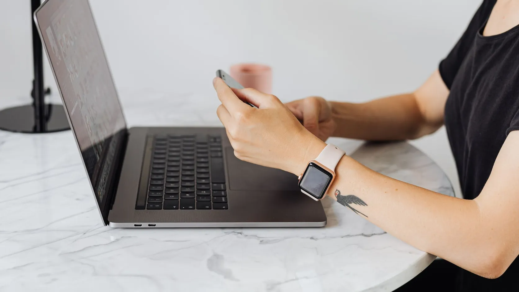 Personne tenant un smartphone à côté d'un ordinateur portable ouvert sur une table en marbre