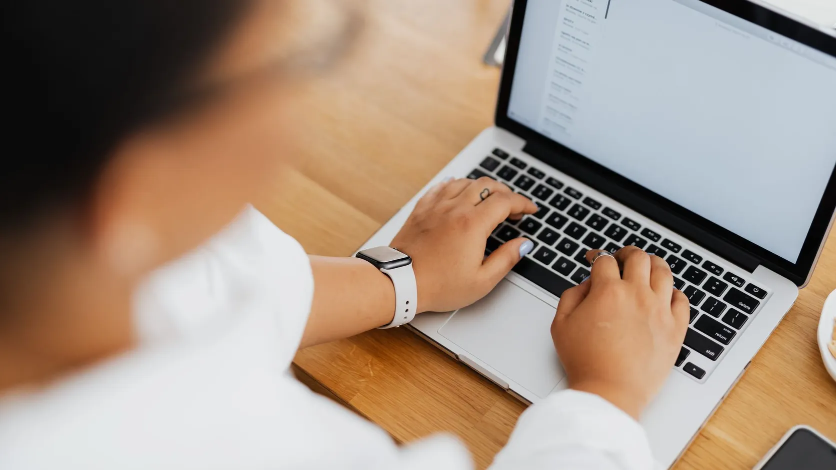 Vue en plongée d'une personne qui tape sur le clavier d'un ordinateur portable posé sur une table en bois